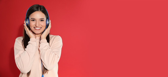 Young woman listening to music with headphones on red background, space for text. Banner design