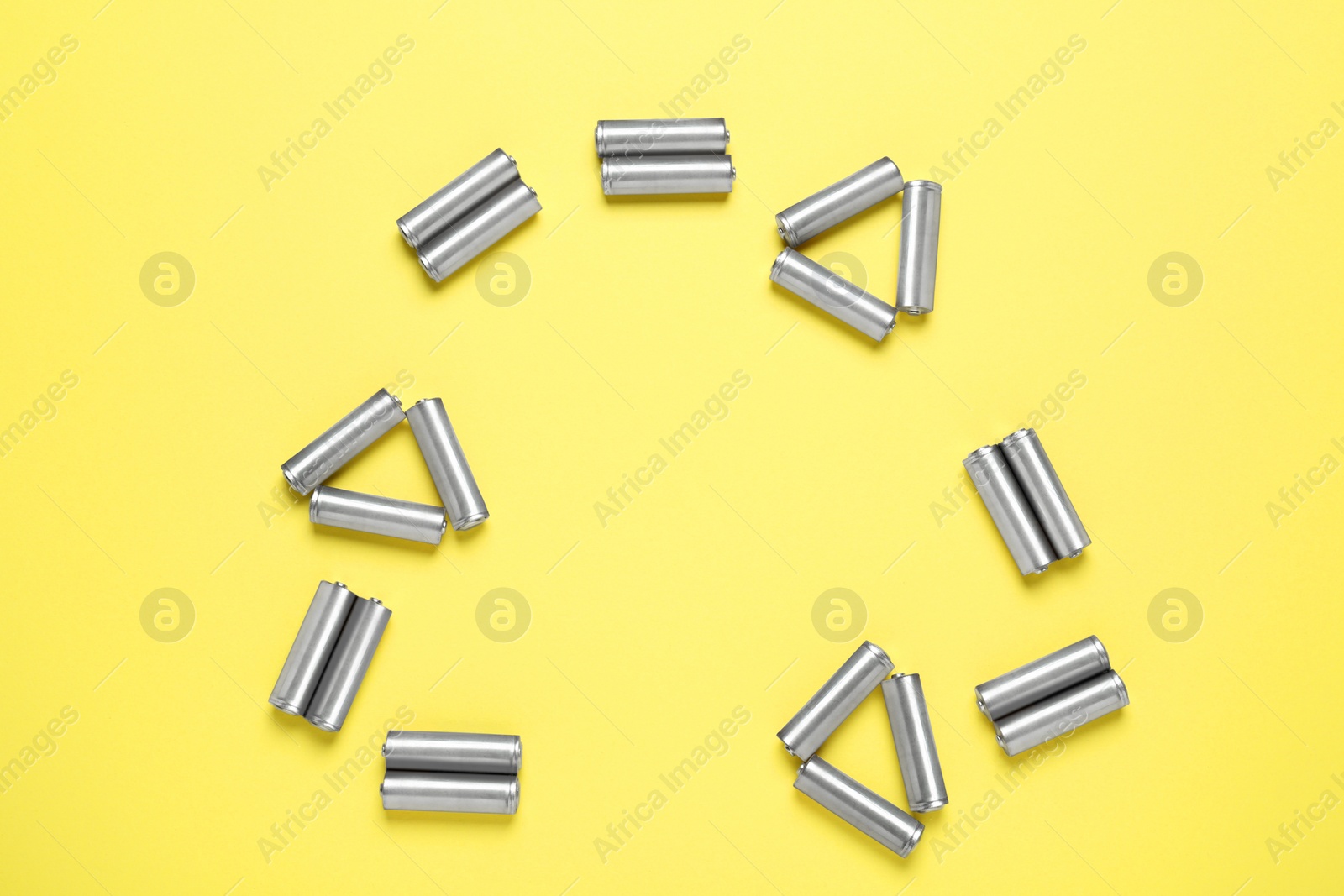 Photo of Recycling symbol made of batteries on yellow background, top view