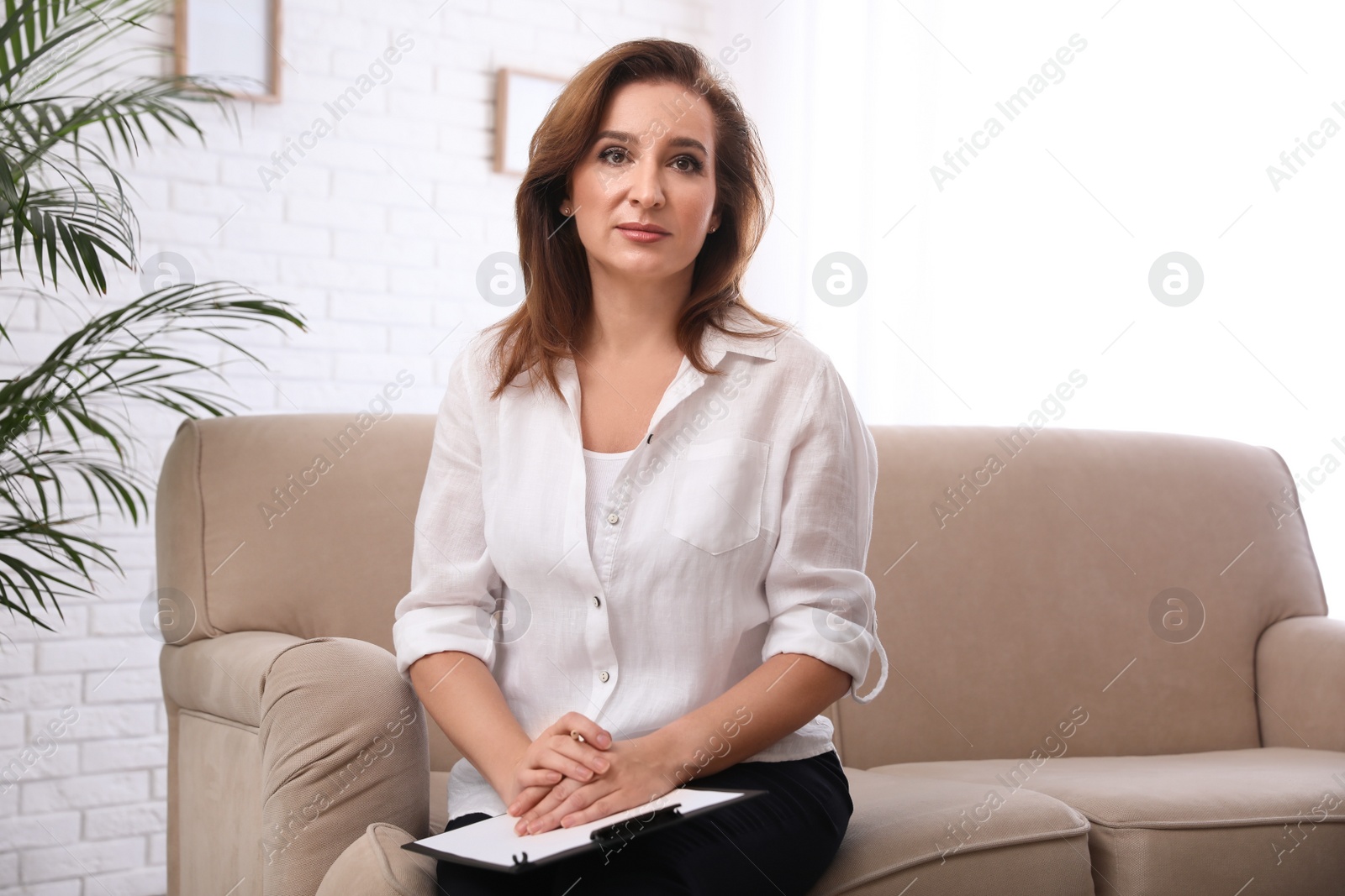 Photo of Portrait of psychotherapist with clipboard on sofa in office