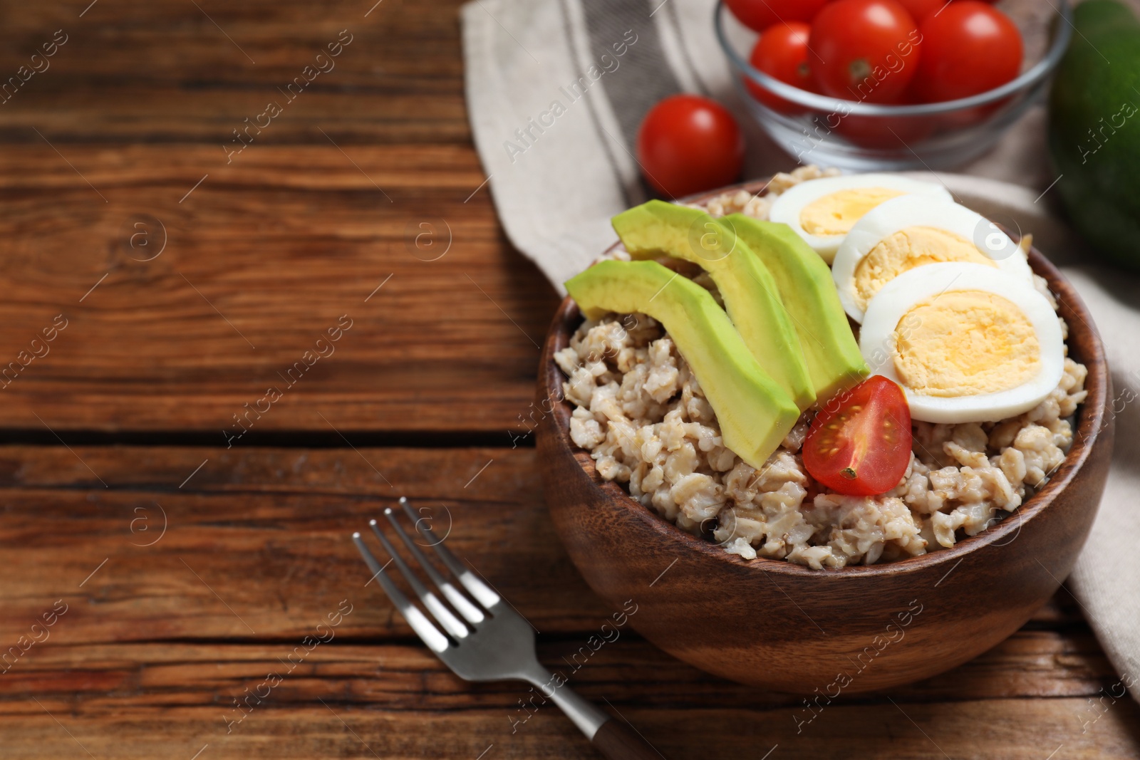 Photo of Tasty boiled oatmeal with egg, avocado and tomato served on wooden table, space for text