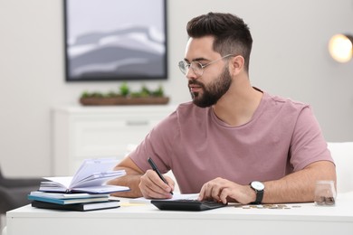 Photo of Young man counting money at white table indoors