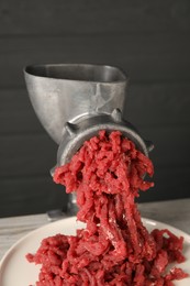 Photo of Metal meat grinder with beef mince on table, closeup