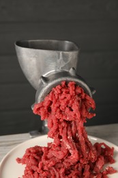 Metal meat grinder with beef mince on table, closeup