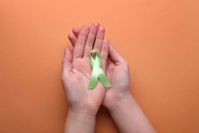 Photo of World Mental Health Day. Woman holding green ribbon on pale orange background, top view