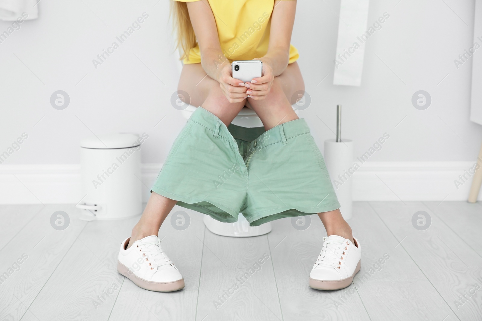 Photo of Young woman using mobile phone while sitting on toilet bowl at home