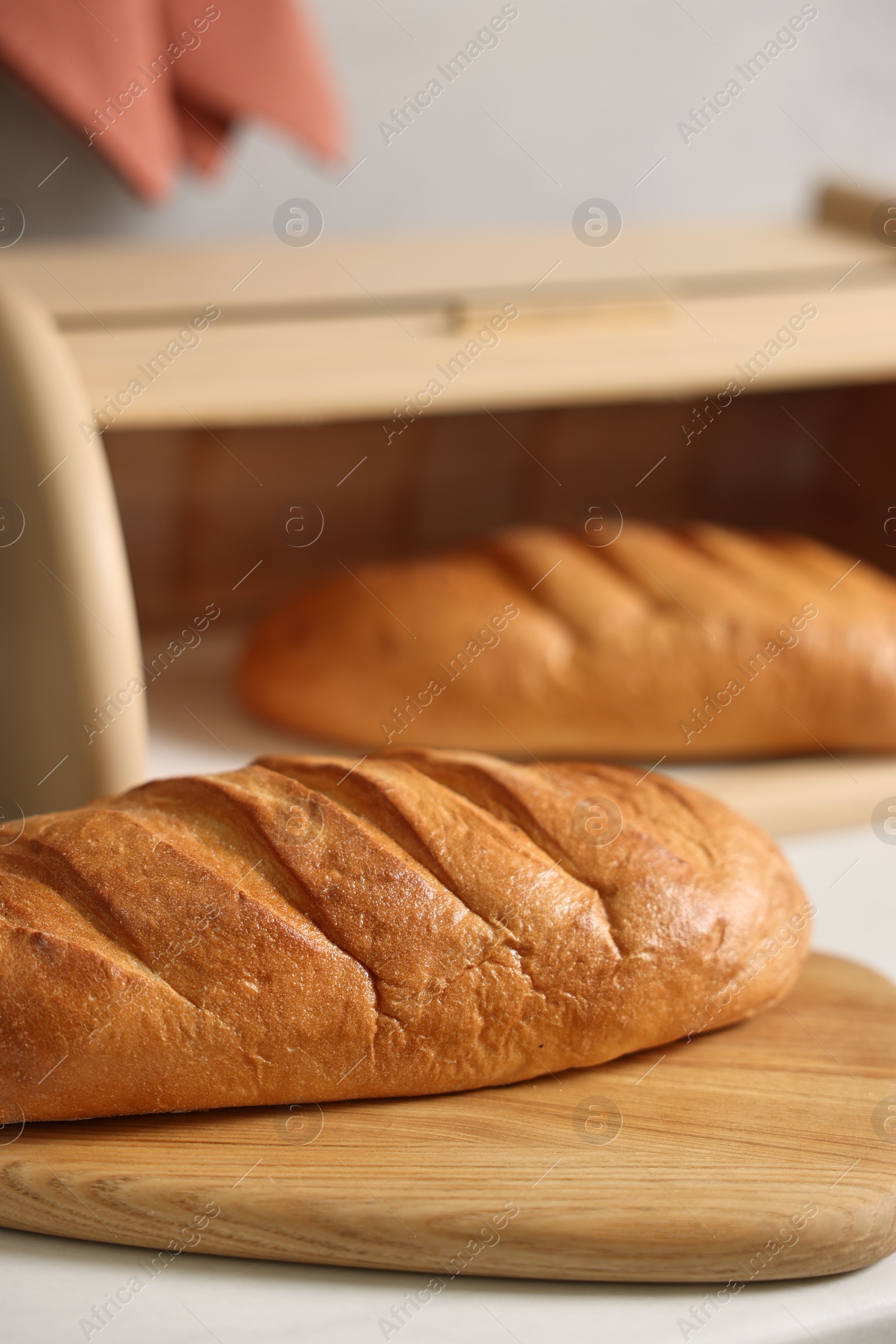 Photo of Wooden bread basket with freshly baked loaves on white marble table in kitchen