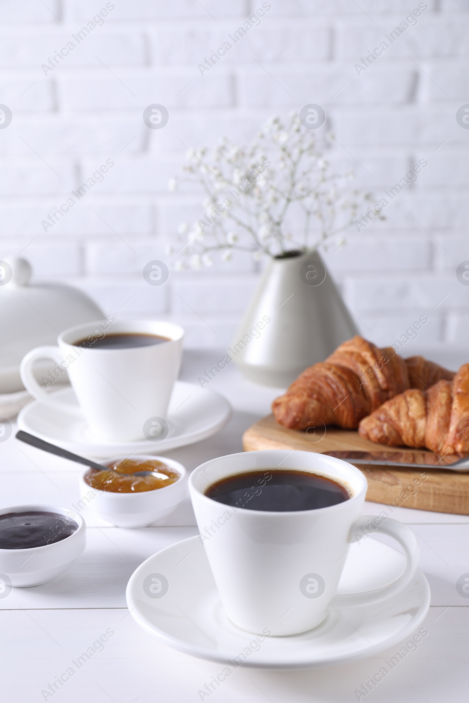 Photo of Cup of coffee, jam and croissants on white wooden table, space for text. Tasty breakfast