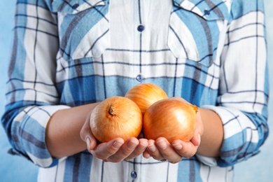 Photo of Woman holding handful of ripe onions on blue background, closeup