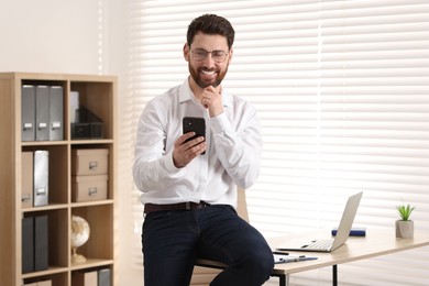 Photo of Portrait of smiling man with smartphone in office