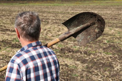 Photo of Man holding shovel in field, back view. Digging process