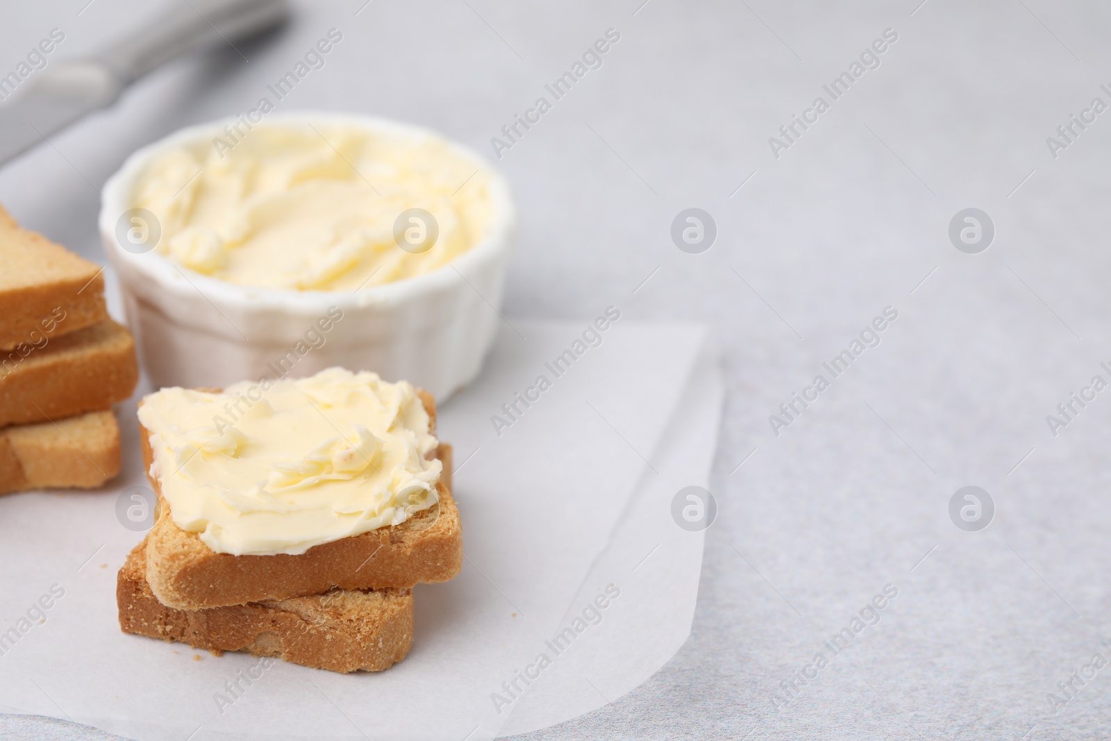Photo of Slices of bread with tasty butter on light gray table, closeup. Space for text