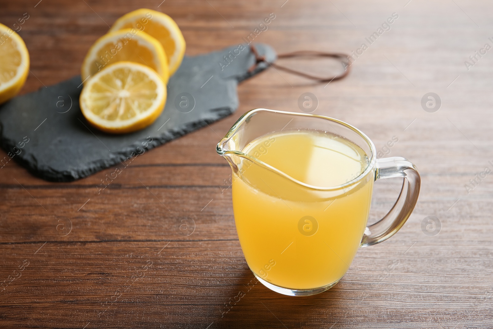 Photo of Glass jug with fresh lemon juice on wooden table