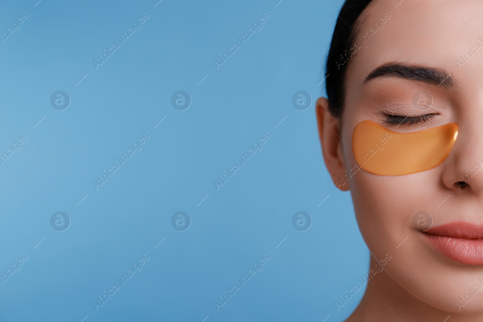 Photo of Beautiful young woman with under eye patch on light blue background, closeup. Space for text