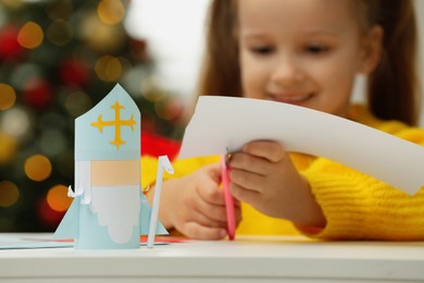 Cute little girl cutting paper at home, focus on Saint Nicholas toy