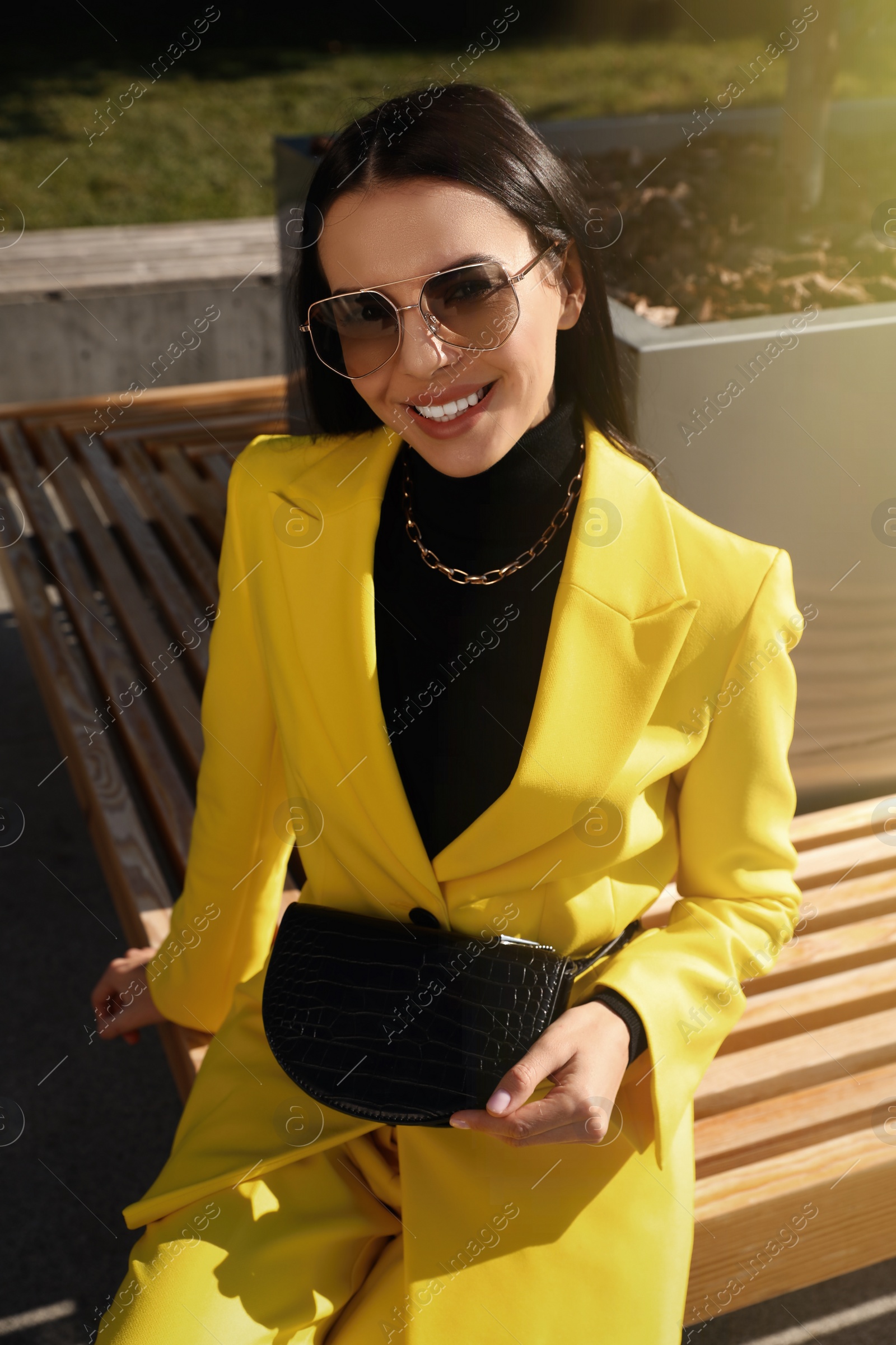 Photo of Beautiful young woman with stylish waist bag sitting on bench outdoors