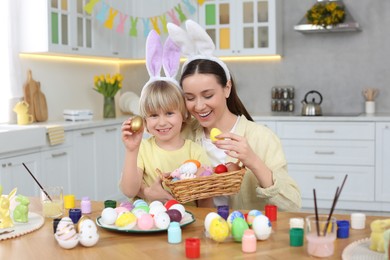 Mother and her cute son with Easter eggs at table in kitchen