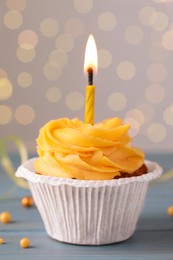 Photo of Tasty birthday cupcake on light blue wooden table against blurred lights, closeup
