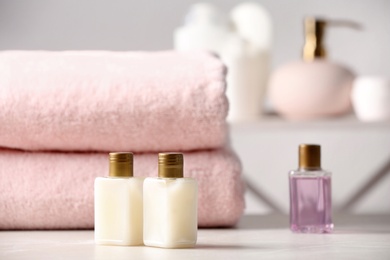 Mini bottles with cosmetic products and towels on table in bathroom, space for text. Hotel amenities