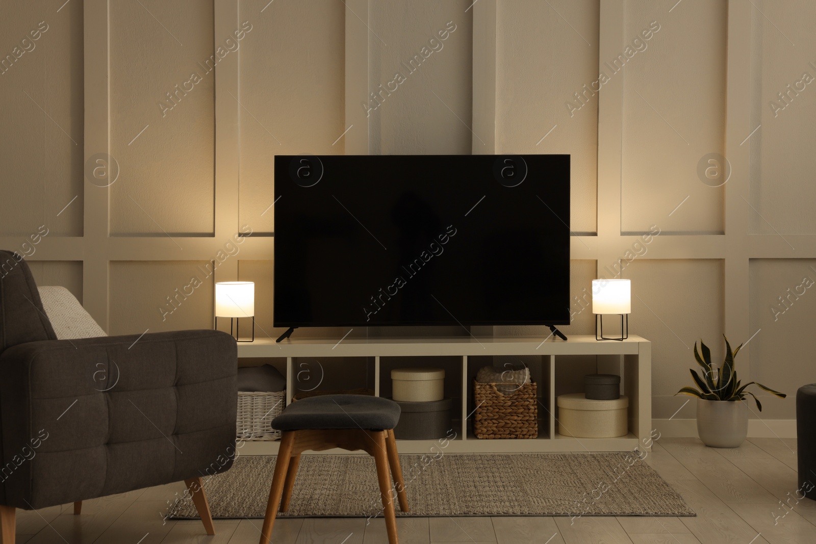Photo of Modern TV on cabinet, armchair and lamps indoors. Interior design