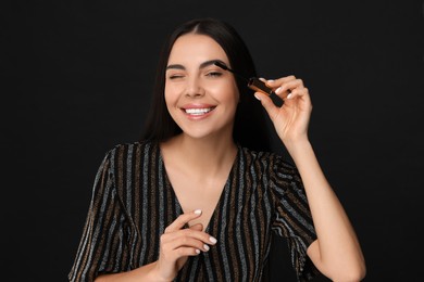 Photo of Beautiful young woman applying mascara on black background