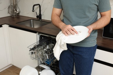 Man wiping plate near open dishwasher in kitchen, closeup