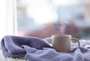 Cup of coffee and knitted sweater near window in morning. Space for text
