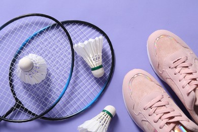 Photo of Feather badminton shuttlecocks, rackets and sneakers on violet background, flat lay