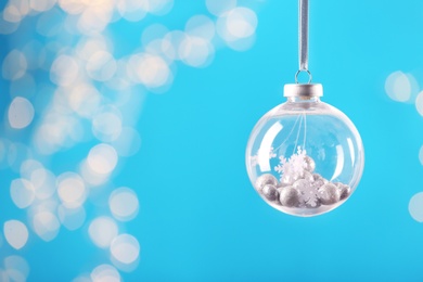 Decorative snow globe hanging on against blurred festive lights, space for text