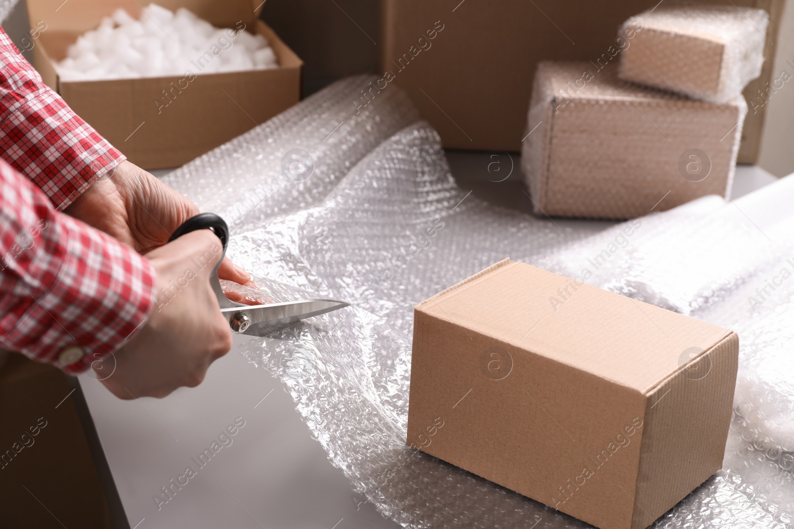 Photo of Woman cutting bubble wrap at table in warehouse, closeup