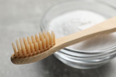 Bamboo toothbrush and bowl of baking soda on grey table, closeup