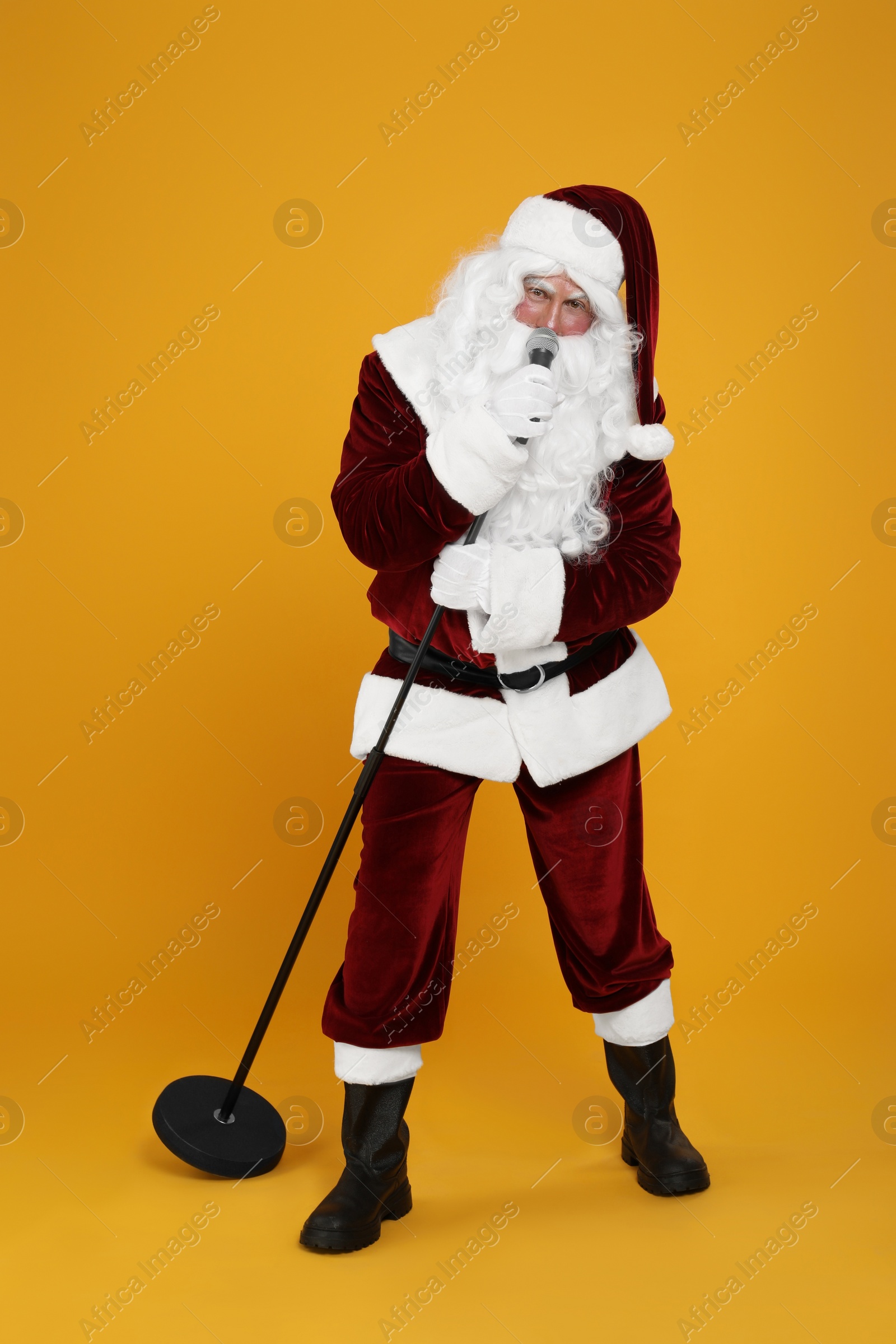 Photo of Santa Claus singing with microphone on yellow background. Christmas music