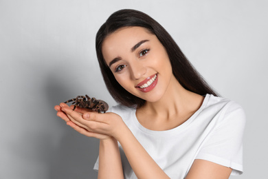 Photo of Woman holding striped knee tarantula on light background. Exotic pet