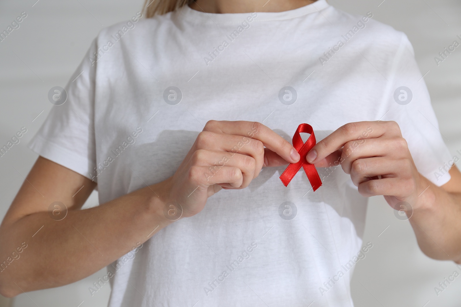 Photo of Woman holding red awareness ribbon on light background, closeup. World AIDS disease day