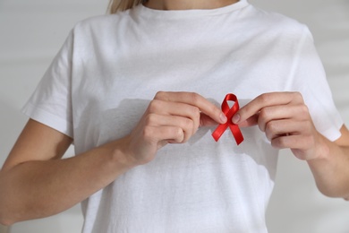 Photo of Woman holding red awareness ribbon on light background, closeup. World AIDS disease day