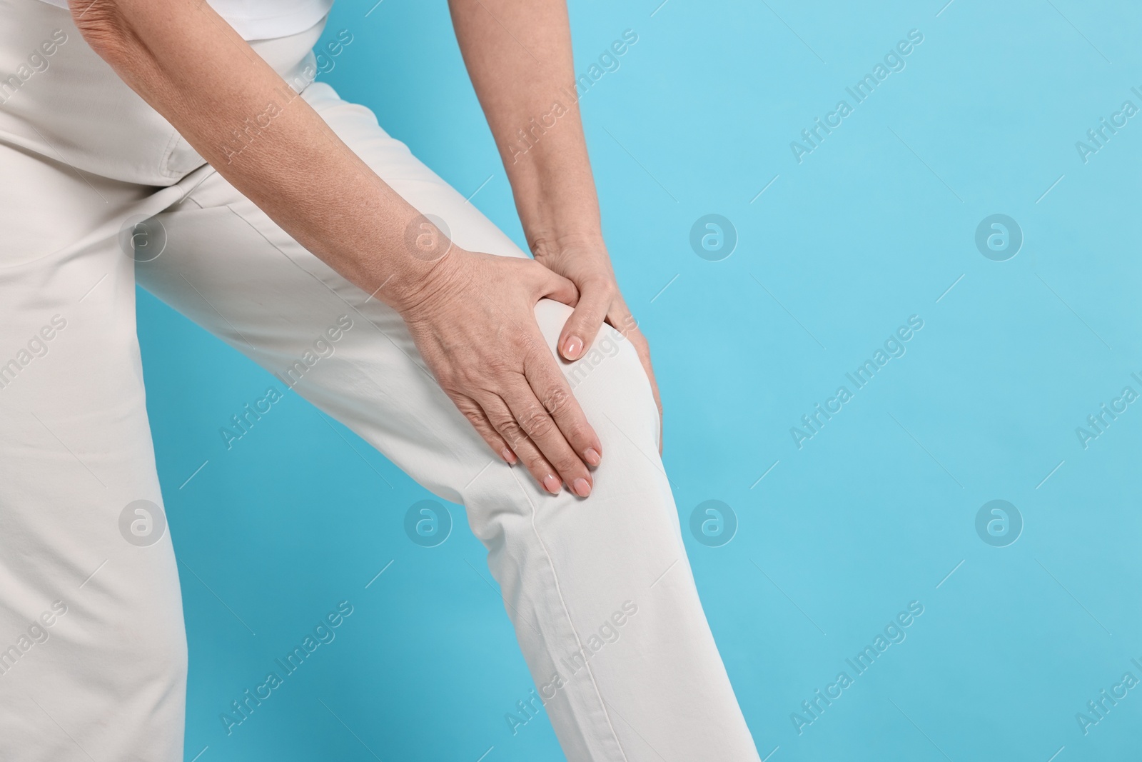 Photo of Arthritis symptoms. Woman suffering from pain in knee on light blue background, closeup. Space for text