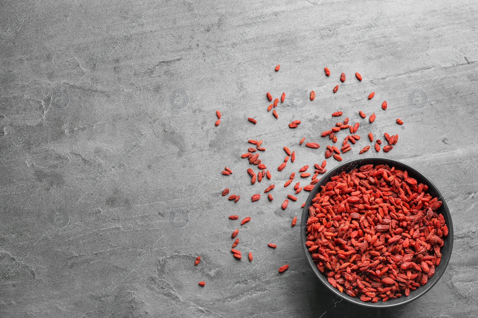 Photo of Bowl of dried goji berries on grey table, top view with space for text. Healthy superfood