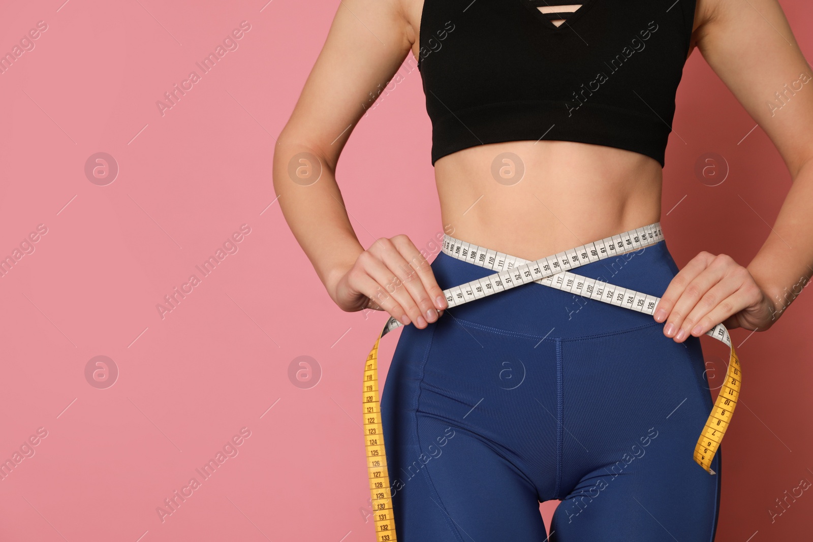 Photo of Woman in sportswear measuring waist with tape on pink background, closeup. Space for text