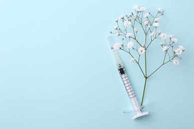 Cosmetology. Medical syringe and gypsophila on light blue background, flat lay. Space for text
