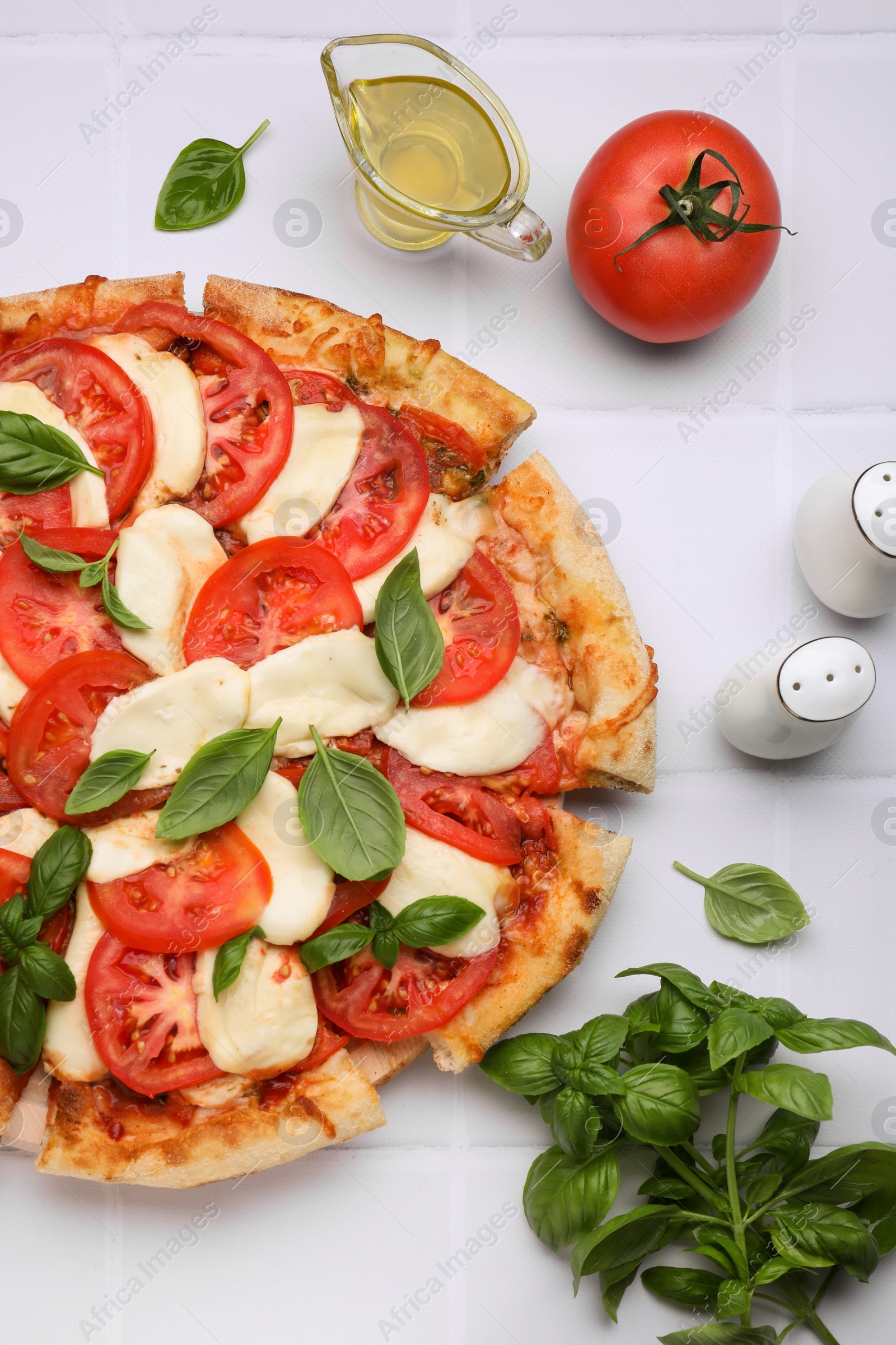 Photo of Delicious Caprese pizza with tomatoes, mozzarella and basil on white tiled table, flat lay