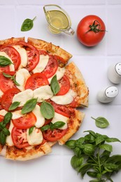 Delicious Caprese pizza with tomatoes, mozzarella and basil on white tiled table, flat lay