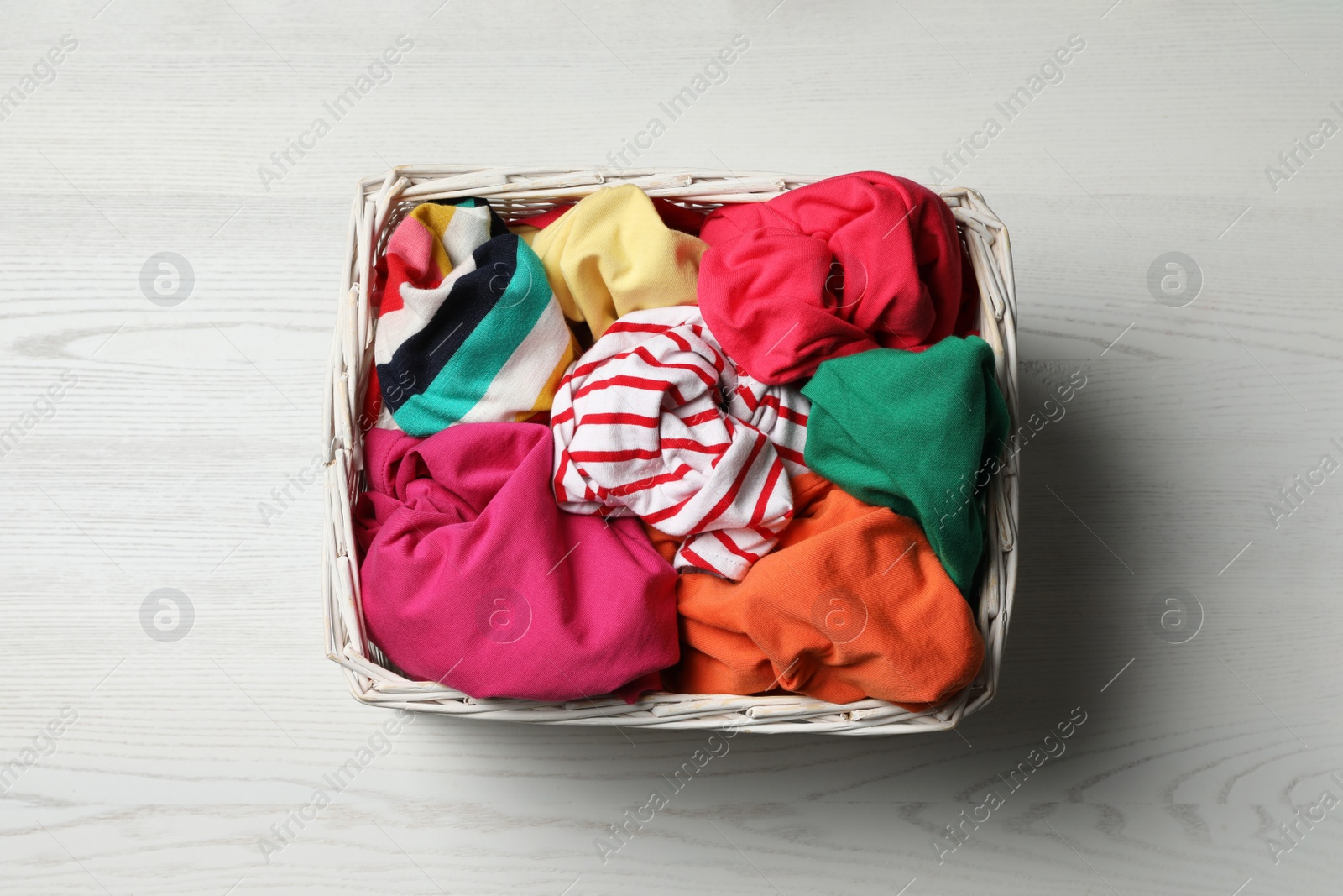 Photo of Wicker basket with laundry on white wooden surface, top view