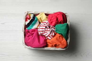 Photo of Wicker basket with laundry on white wooden surface, top view
