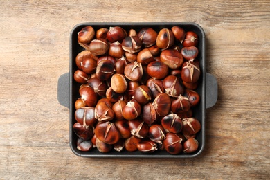 Photo of Delicious roasted edible chestnuts in baking dish on wooden table, top view