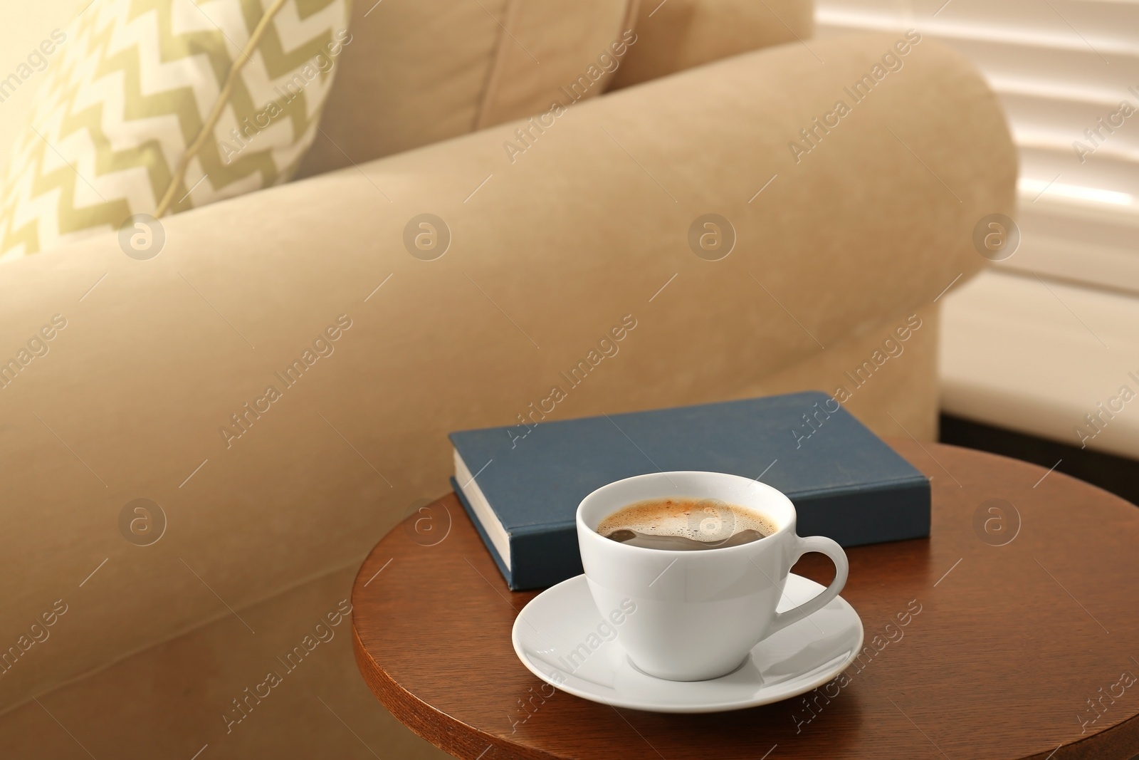 Photo of Cup of coffee and book on table near sofa in room