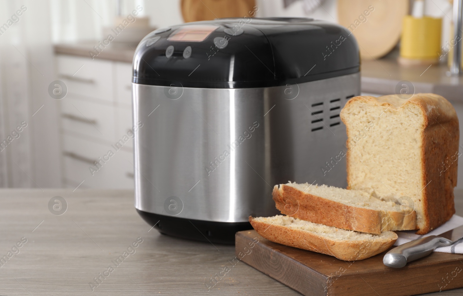 Photo of Breadmaker and cut homemade bread on wooden table in kitchen. Space for text