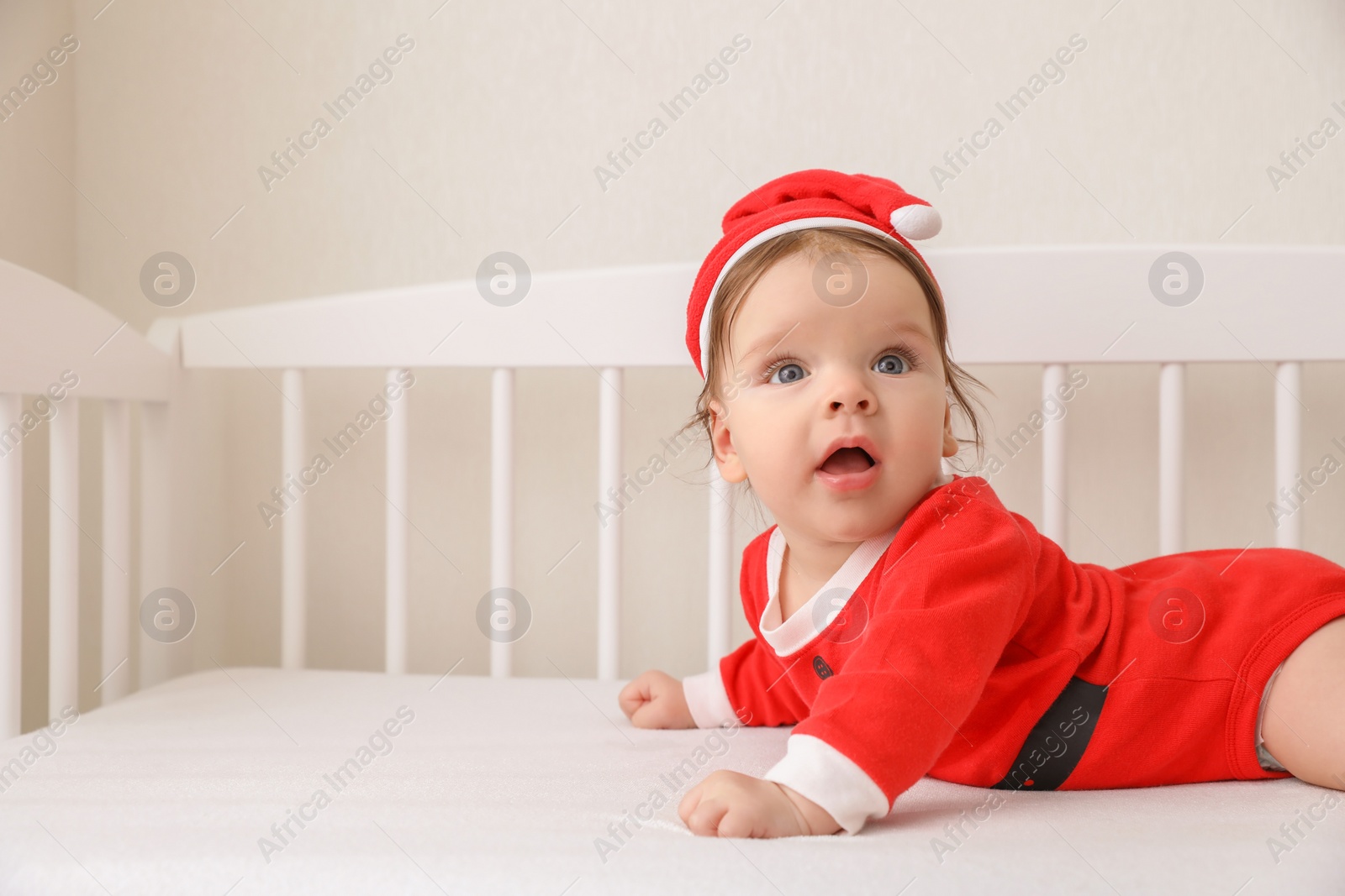 Photo of Cute baby wearing festive Christmas costume in crib. Space for text