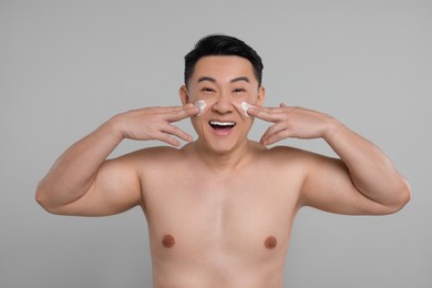 Photo of Handsome man applying cream onto his face on light grey background