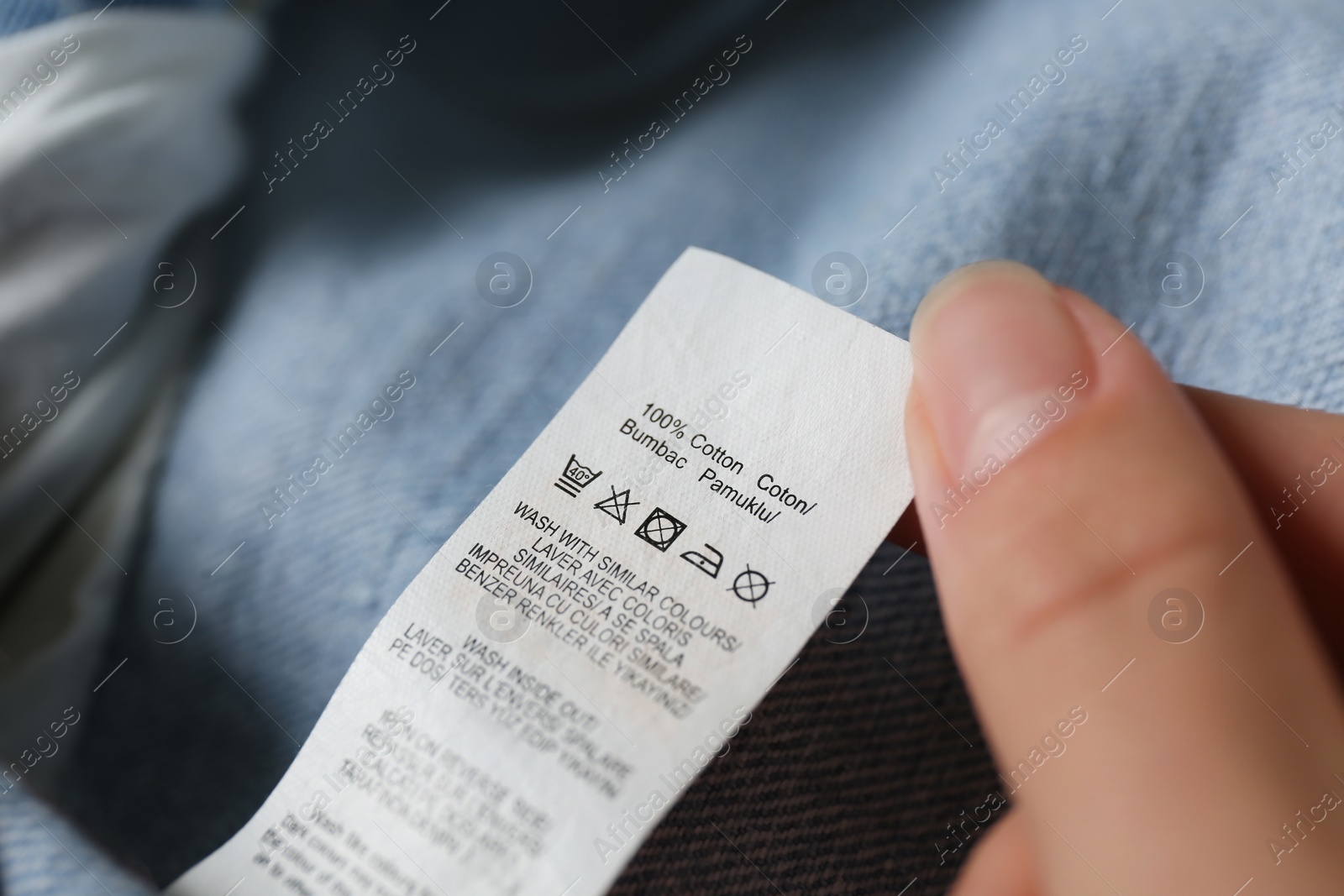 Photo of Woman reading clothing label with care symbols and material content on jeans, closeup