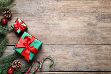 Gift boxes, candy canes, fir tree branches and Christmas decor on wooden table, flat lay. Space for text