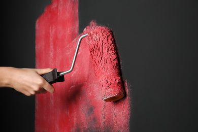 Photo of Woman painting grey wall with pink dye, closeup